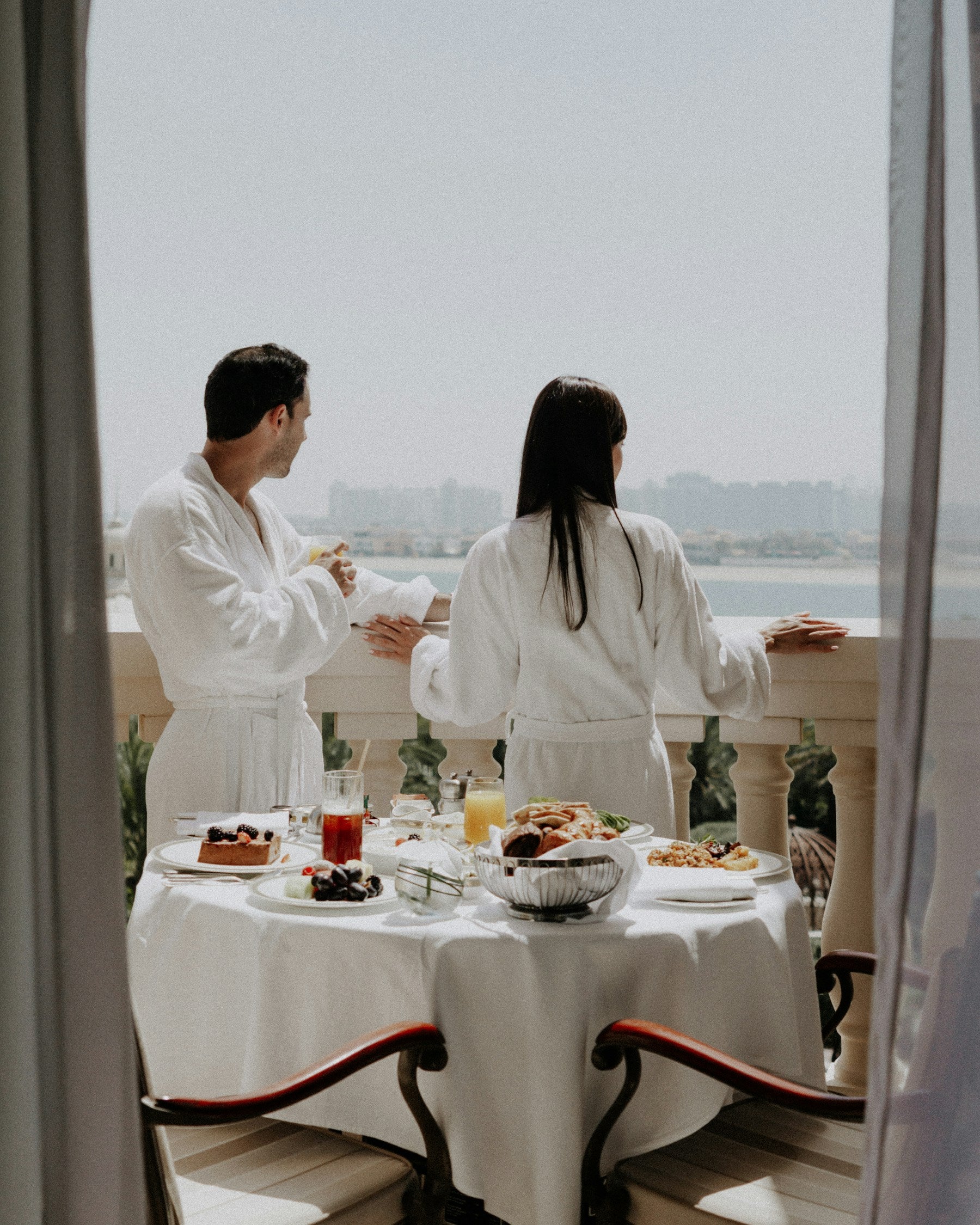 Two guests in robes sharing breakfast on a balcony overlooking the water