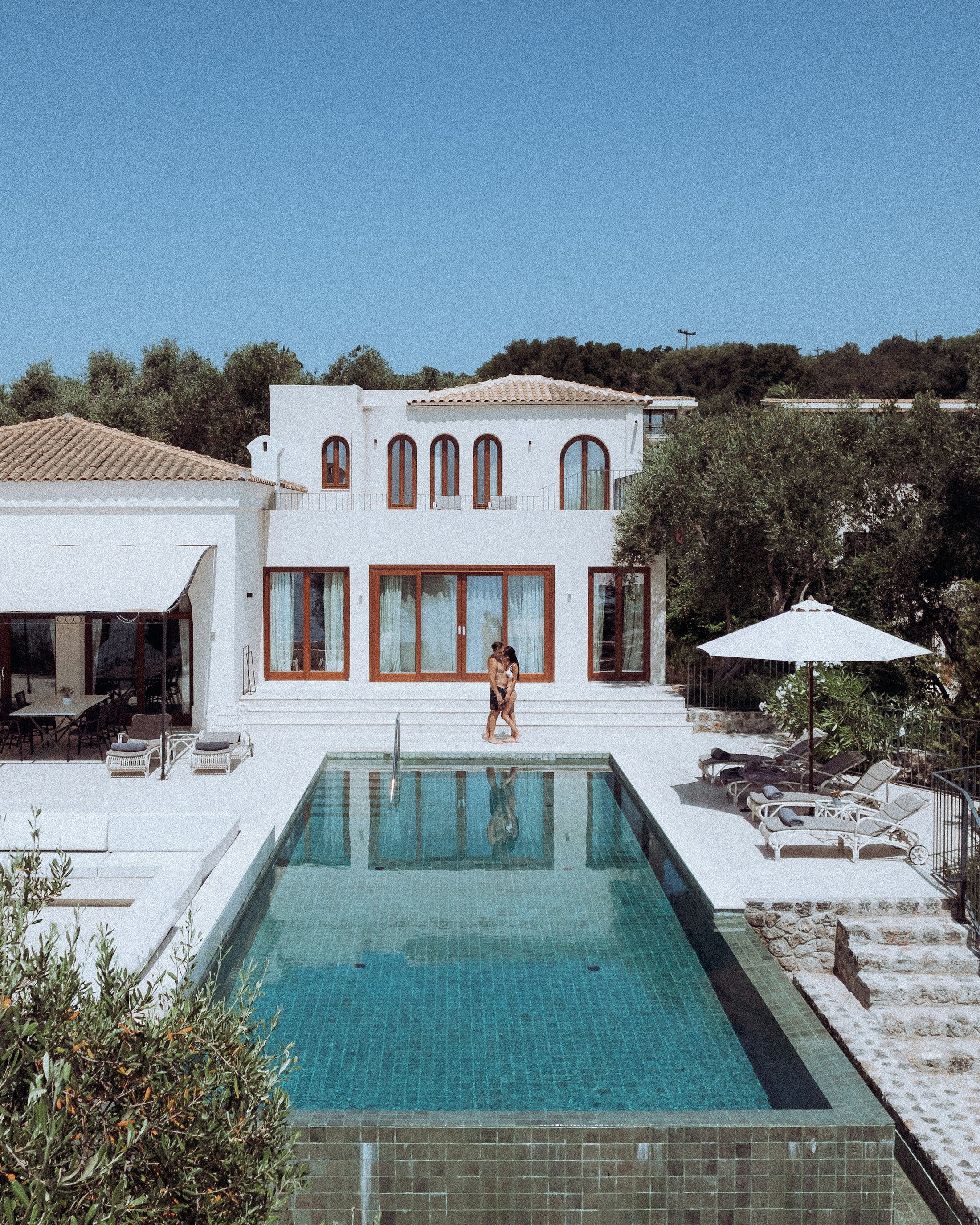 White Mediterranean villa with a long turquoise pool and two guests